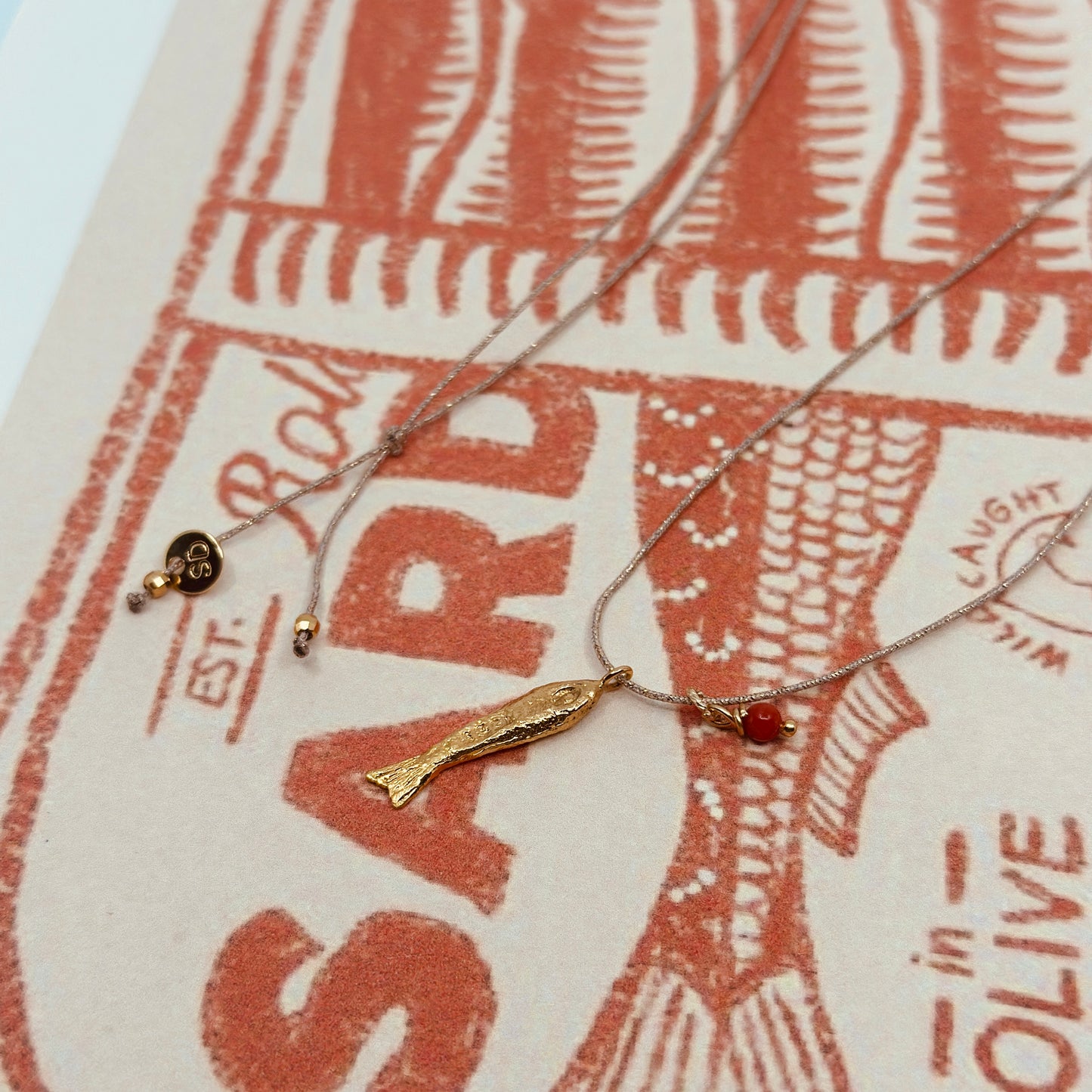 Ketting van luxe goudkleurig koord met een klein verguld sardientje en koraal